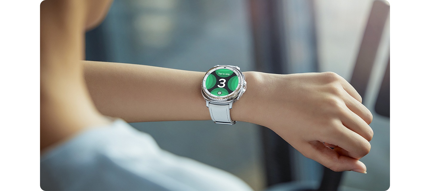 화이트 색상의 하이브리드 밴드가 장착된 갤럭시 워치8 클래식을 착용한 사람이 손목을 들어 워치 페이스를 확인합니다.