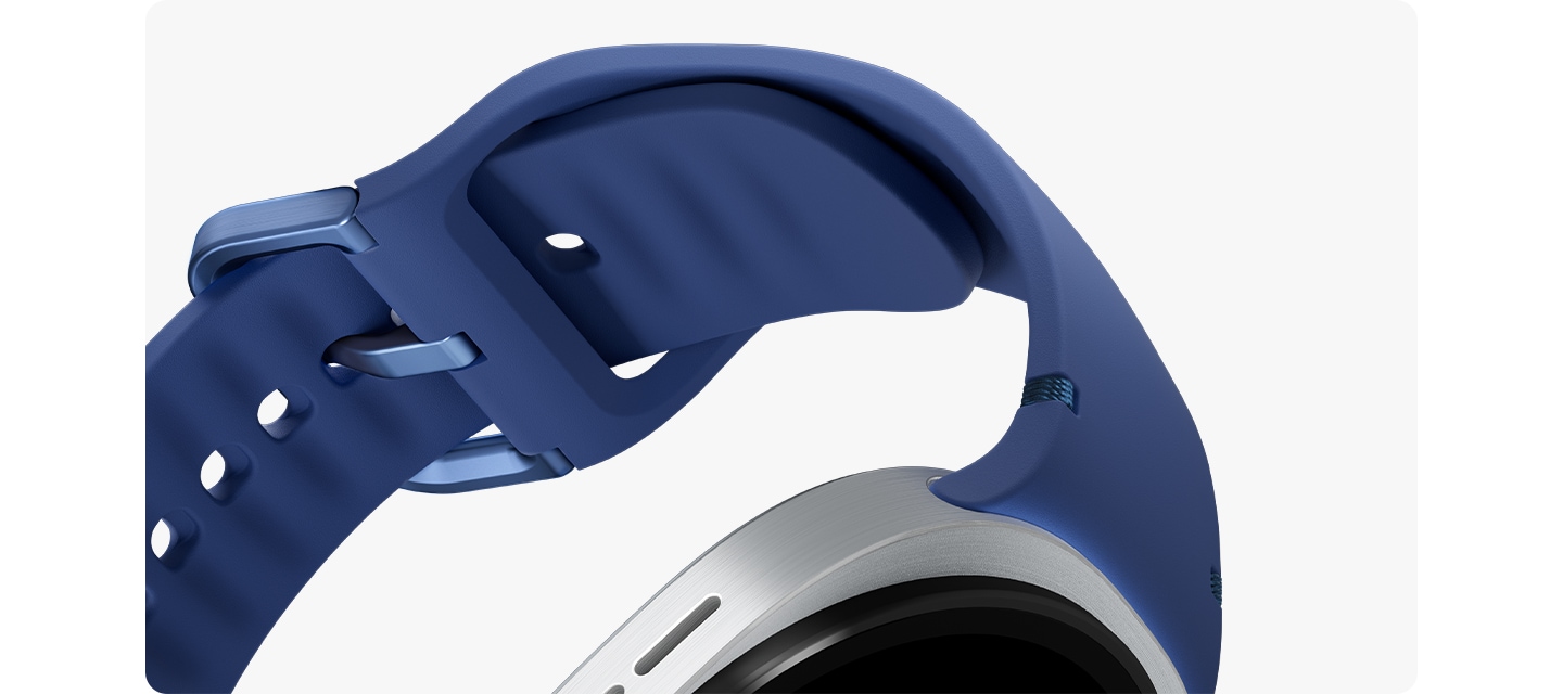 블루 색상의 갤럭시 워치8 스포츠 밴드가 기울어져 있고, 클로즈업하여 부드러운 고무 소재를 강조합니다. 스포츠 밴드는 버클이 잠긴 채로 갤럭시 워치8에 장착되어 둥근 원을 이룹니다.