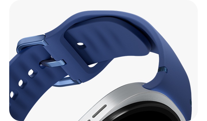 블루 색상의 갤럭시 워치8 스포츠 밴드가 기울어져 있고, 클로즈업하여 부드러운 고무 소재를 강조합니다. 스포츠 밴드는 버클이 잠긴 채로 갤럭시 워치8에 장착되어 둥근 원을 이룹니다.