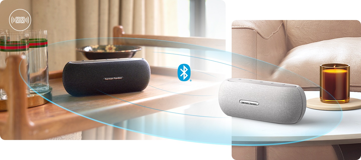 스피커 두 대가 블루투스 페이링으로 연결되어 있습니다. 왼쪽에는 블랙 색상의 스피커가 이동식 트레이 위에 놓여 있습니다. 스피커 왼쪽에는 유리잔들이 있으며, 스피커 뒤에는 접시가 놓여 있습니다. 오른쪽에는 테이블 위에 스피커가 놓여 있습니다. 스피커 뒤로는 향초와 소파가 보입니다.