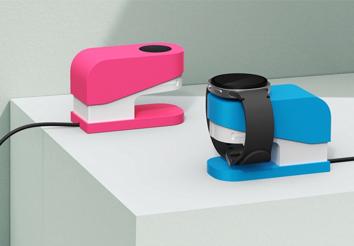 사각진 조형물 구석에 충전독을 장착한 스테이플러 갤럭시 워치 충전독 거치대가 보이고 있으며, 파란색 충전독 거치대에는 워치가 충전되고 있는 모습이 보입니다.