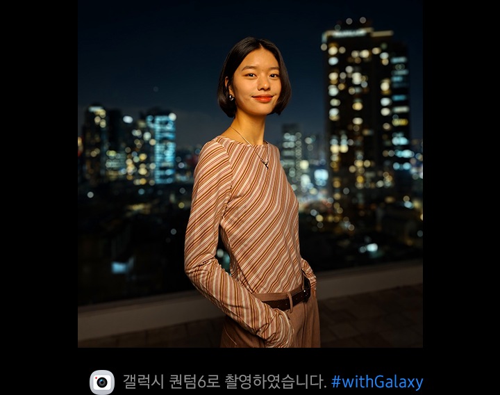 도시의 야경을 배경으로 한 사람이 카메라를 향해 미소 짓고 있습니다. 이미지 하단에는 카메라 아이콘과 함께 'Captured by Galaxy A56 5G' 문구와 '#withGalaxy' 해시태그가 있습니다.