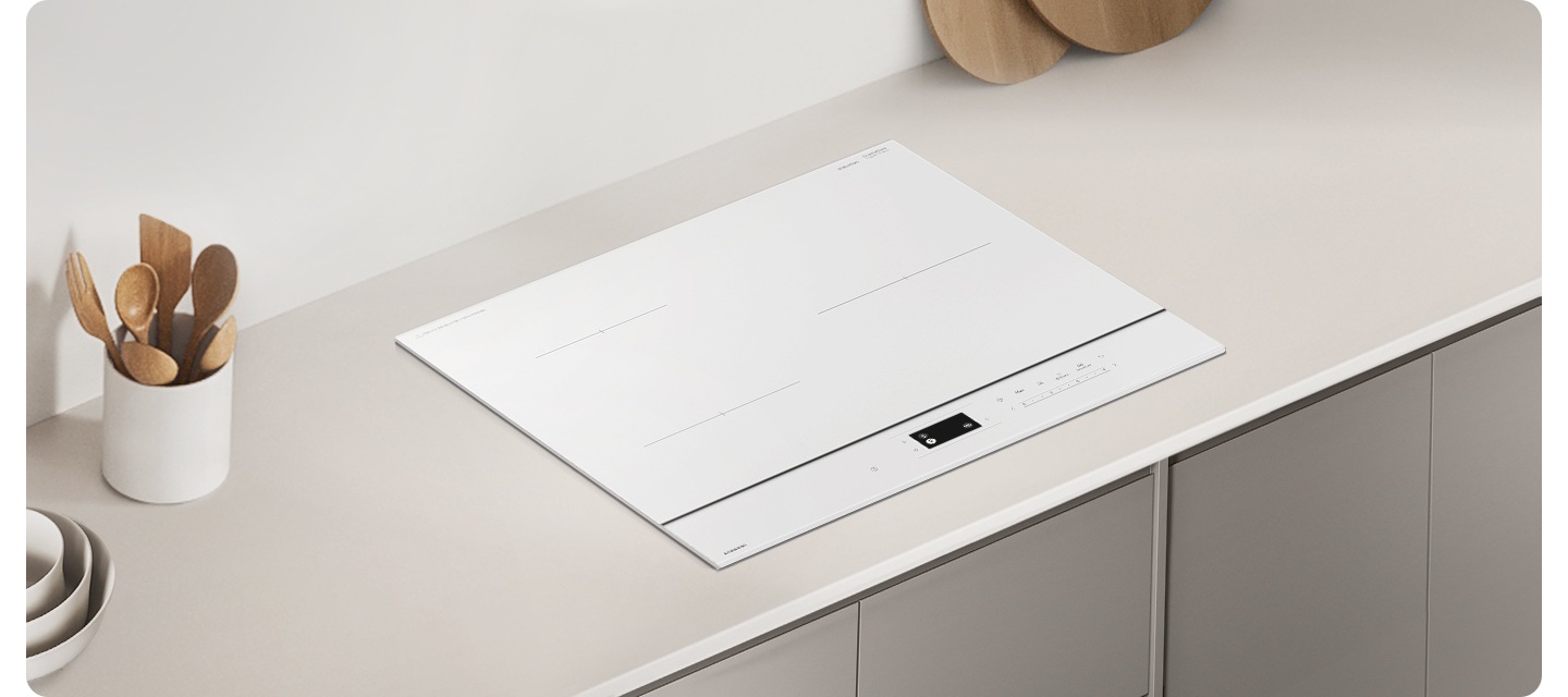 그레이톤 우드 패널에 그레이 톤 대리석 상판이 깔린 주방 테이블이 보입니다. 테이블 가운데에는 인덕션이 설치되어 있습니다. 인덕션 오른쪽에는 흰색 원통 모양의 도자기 수저 통 안에 원목 수저가 꽂혀 있고 왼쪽 상단 부분에는 나무 도마 하단 부분이 보이고 있습니다.