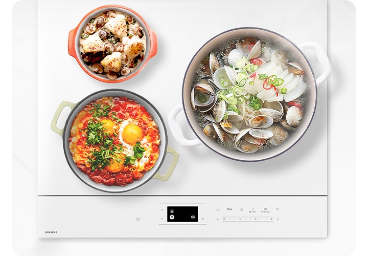 흰색대리석 상판 위 인덕션이 정면으로 보입니다. 화구에는 크기가 다른 3개의 냄비에 음식물이 가득 들어있는 상태로 올려져 있습니다. 우측 대화구에는 가장 큰 흰색 냄비와 조개와 무가 가득 들은 조개탕이 펄펄 끓고 있는 모습입니다. 플렉스 존 상단에는 가장 작은 사이즈의 오렌지색 냄비와 크림수프가 완성되어 있습니다. 플렉스 존 하단에는 중간 사이즈의 연두색 냄비에 에그인 헬이 완성되어 있습니다. 전기레인지 오른쪽에는 흰색 도자기 그른 안에 나무 주걱이 들어 있습니다.