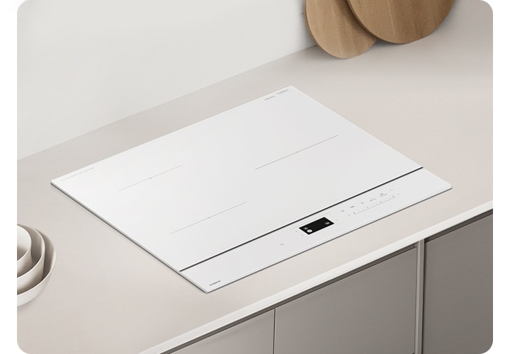 그레이톤 우드 패널에 그레이 톤 대리석 상판이 깔린 주방 테이블이 보입니다. 테이블 가운데에는 인덕션이 설치되어 있습니다. 인덕션 오른쪽에는 흰색 원통 모양의 도자기 수저 통 안에 원목 수저가 꽂혀 있고 왼쪽 상단 부분에는 나무 도마 하단 부분이 보이고 있습니다.