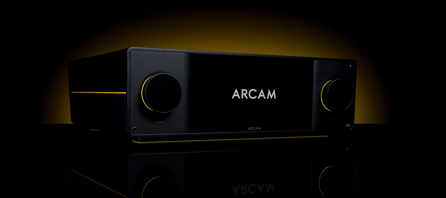 어두운 공간에 AV 리시버가 놓여 있습니다. AV 리시버 뒤에는 노란색 불빛이 보입니다.