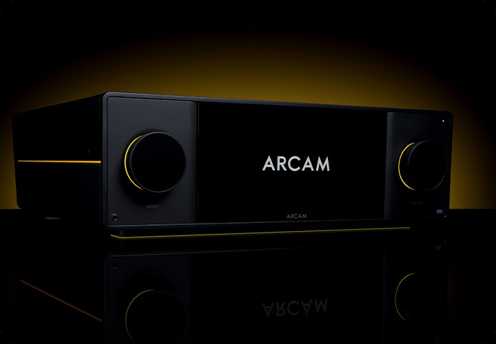 어두운 공간에 AV 리시버가 놓여 있습니다. AV 리시버 뒤에는 노란색 불빛이 보입니다.