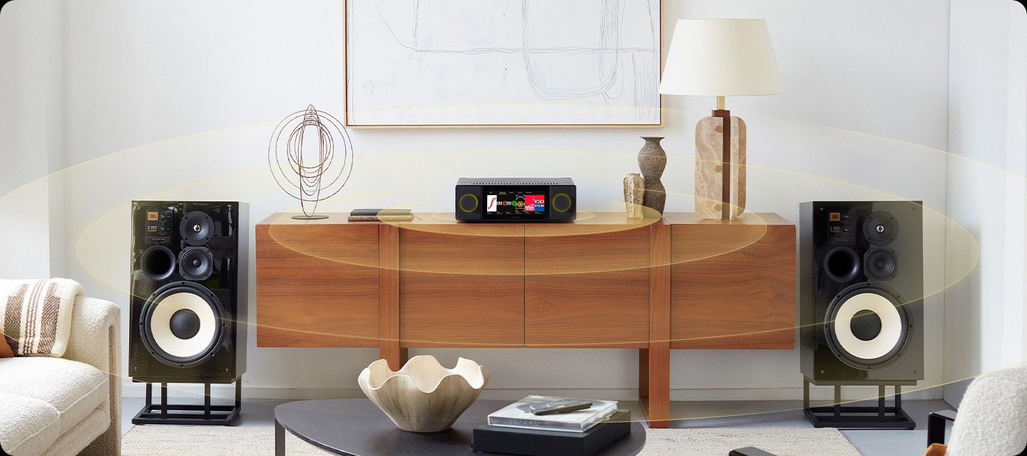 장식장 위에 AV 리시브가 놓여 있으며, 장식장 양옆에는 스탠드 위에 스피커가 놓여 있습니다. 스피커에서 음향효과가 나오고 있습니다. 