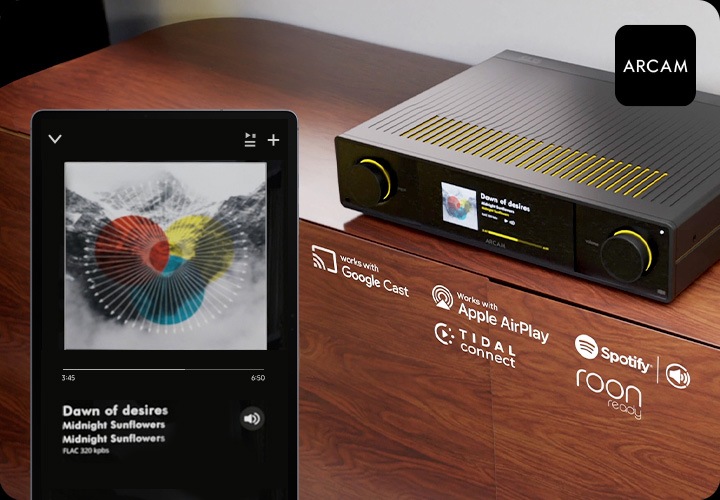 장식장 위에 AV 리시버가 놓여 있습니다. 장식장에는 Google Cast, Apple AirPlay, Spotify Connect, Tidal Connect, Roon ready 로고가 있습니다. 장식장 왼쪽 앞에는 스마트폰이 있으며, 음악이 스트리밍 되는 중입니다.