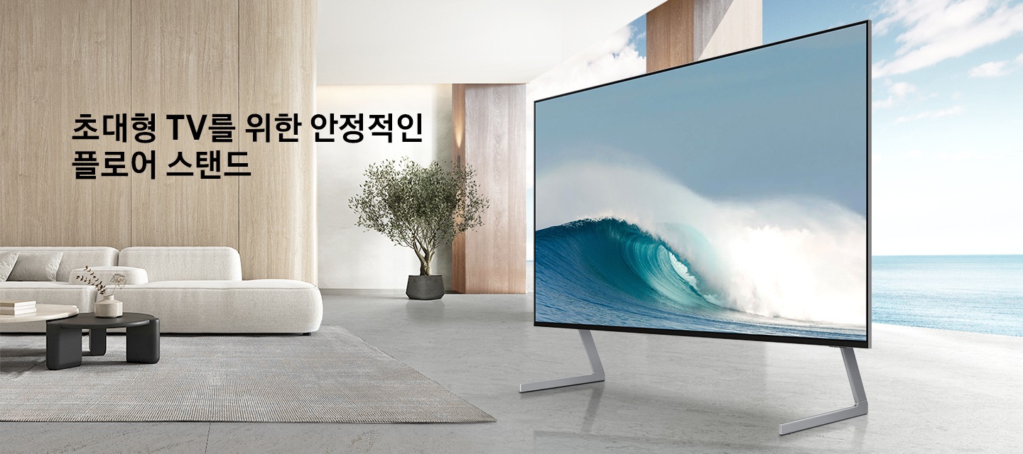 거실에 플로어 스탠드가 장착된 TV가 놓여 있습니다. TV 화면에는 파도가 지고 있습니다. 초대형 TV를 위핝 안정적인 플로어 스탠드 KV입니다.