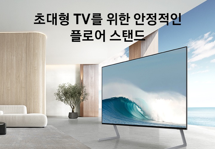 거실에 플로어 스탠드가 장착된 TV가 놓여 있습니다. TV 화면에는 파도가 지고 있습니다. 초대형 TV를 위핝 안정적인 플로어 스탠드 KV입니다.