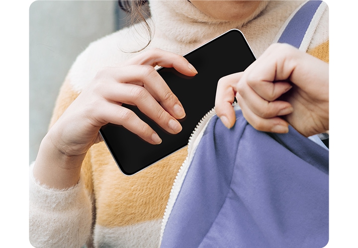 [터틀넥을 입은 여성이 ÁR 필름을 부착한 갤럭시 S25 F~É를 가방에 넣고 있습니다.]