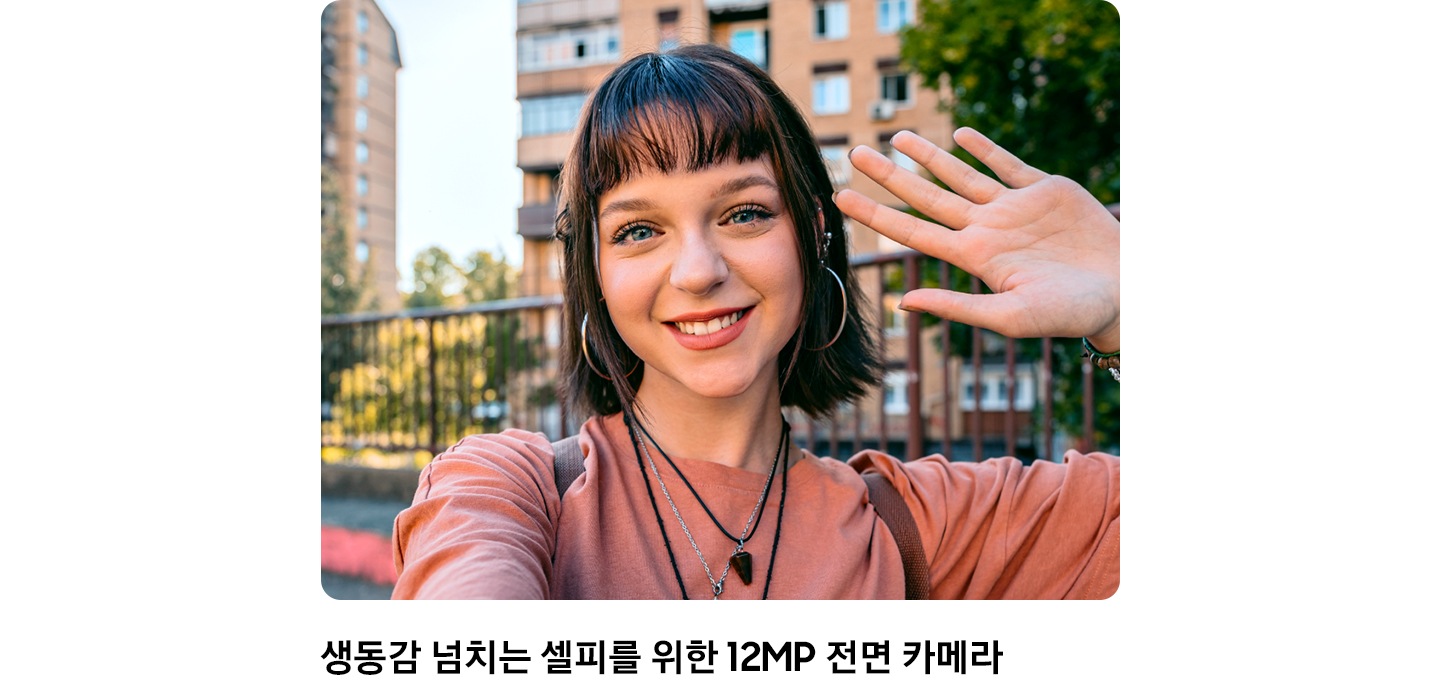 [복숭아색 셔츠와 여러 개의 목걸이를 착용한 사람이 야외에서 셀카를 찍고 있습니다. 전면 카메라의 놀라운 셀카 촬영 능력을 강조합니다.]