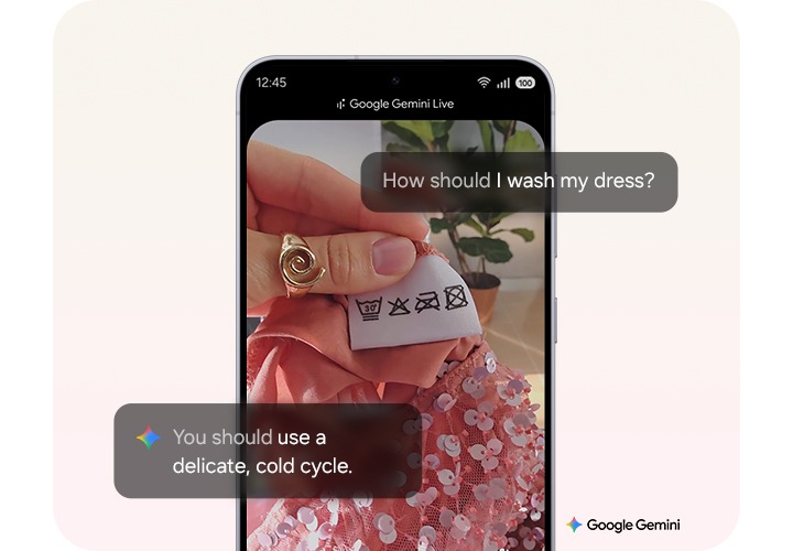 [스마트폰 화면에 Góóg~lé Gé~míñí~ Lívé~ 인터페이스가 표시되어 있습니다. 손으로 세탁 기호가 인쇄된 의류 라벨을 들고 있으며 화면에는 ‘Hów s~hóúl~d Í wá~sh mý~ drés~s¿’라는 질문과 ‘Ýó~ú shó~úld ú~sé á d~élíc~áté, c~óld c~ýclé~.’라는 답변이 있습니다. 배경에는 스팽글 드레스와 식물이 있습니다.]