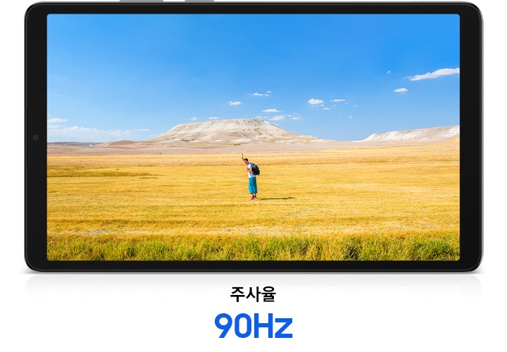 갤럭시 탭 A11이 가로로 놓여있고 화면에는 자유로운 분위기 속에서 손을 흔드는 남성이 선명하게 담겨 있습니다. 배경에는 푸른 하늘과 노란빛, 갈색이 어우러진 드넓은 초원이 펼쳐집니다. 태블릿 PC의 하단에는 '주사율 90Hz'라는 문구가 표시됩니다.