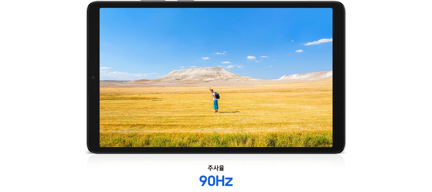 갤럭시 탭 A11이 가로로 놓여있고 화면에는 자유로운 분위기 속에서 손을 흔드는 남성이 선명하게 담겨 있습니다. 배경에는 푸른 하늘과 노란빛, 갈색이 어우러진 드넓은 초원이 펼쳐집니다. 태블릿 PC의 하단에는 '주사율 90Hz'라는 문구가 표시됩니다.