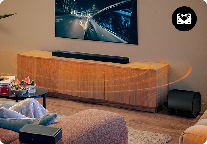 여성이 소파에 앉아서 TV를 보고 있습니다. TV 아래에는 장식장이 놓여 있으며, 장식장 위에는 사운드바가 놓여 있고 장식장 오른쪽에는 우퍼가 놓여 있습니다. 사운드바와 우퍼에서 음향효과가 나오고 있습니다.