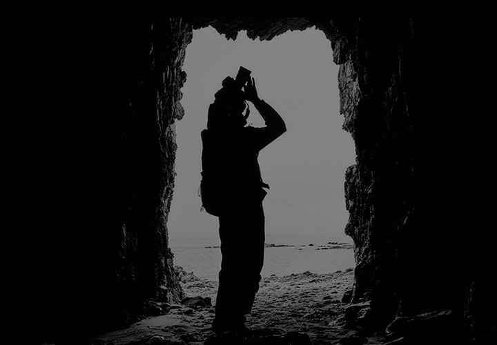 어두운 동굴에서 카메라로 사진을 찍고 있는 사람의 실루엣이 드러나는 이미지 입니다.