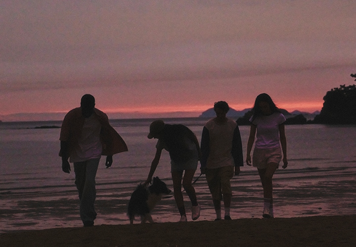 붉은 노을이 지고 있는 바다를 배경으로 사람 네 명과 강아지 한 마리가 앞으로 걸어나오고 있는 듯한 이미지 입니다.
