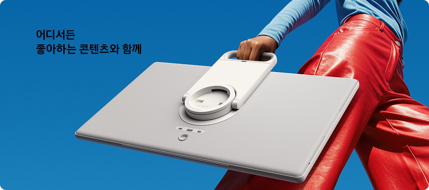 여성이 스탠드에서 분리된 The Movingstyle을 들고 이동하고 있습니다. 좌측 상단에는 '어디서든 좋아하는 콘텐츠와 함께' 문구가 기재되어 있습니다.