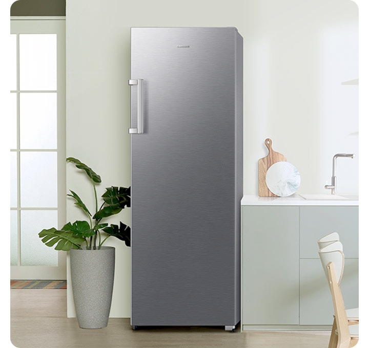 연한 그린톤 주방에 리파인드 이녹스 냉동고가 설치되어 있습니다. 냉동고 좌측에는 큰 화분이 놓여있으며, 우측으로는 하부장이 보입니다.