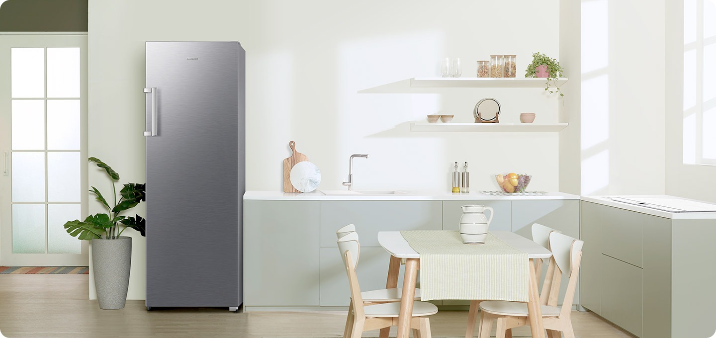 연한 그린톤 주방에 리파인드 이녹스 냉동고가 설치되어 있습니다. 냉동고 좌측에는 큰 화분이 놓여있으며, 우측으로는 하부장이 보입니다.