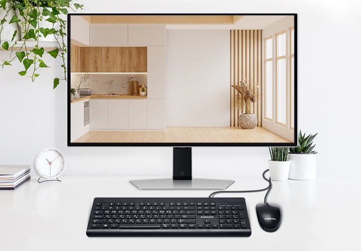 화이트톤의 책상 중앙에 모니터가 있고 모니터 앞에는 유선 키보드와 마우스가 있습니다. 모니터 양쪽으로는 화분으로 꾸며져 있습니다.
