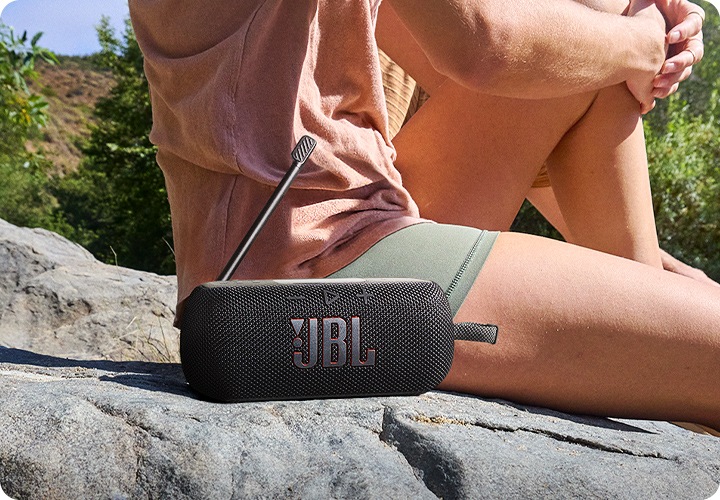 바위 위에 사람이 앉아 있습니다. 그 옆에는 블랙 색상의 라디오 스피커가 놓여 있습니다.