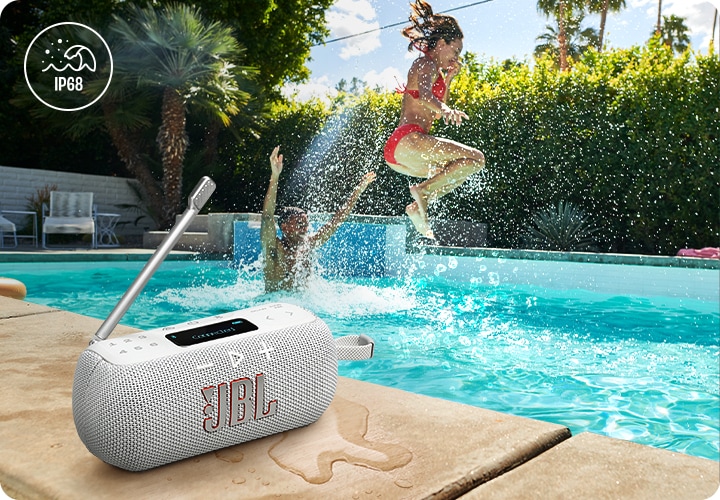 수영장 테두리석에 화이트 색상의 라디오 스피커가 놓여 있습니다. 그 뒤로는 물놀이를 하는 사람들이 있습니다.