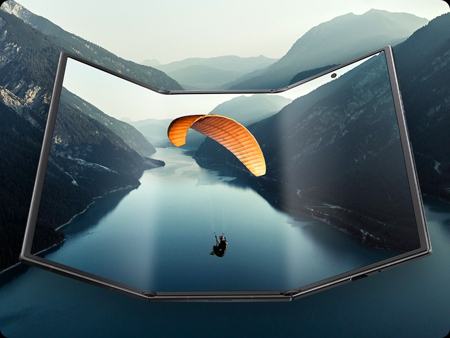 갤럭시 Z 트라이폴드가 거의 펼쳐진 상태로 넓은 메인 디스플레이를 드러냅니다. 화면에는 풍경 이미지가 표시되며 이미지는 기기 밖으로 이어져 영화 같은 장면을 강조합니다.