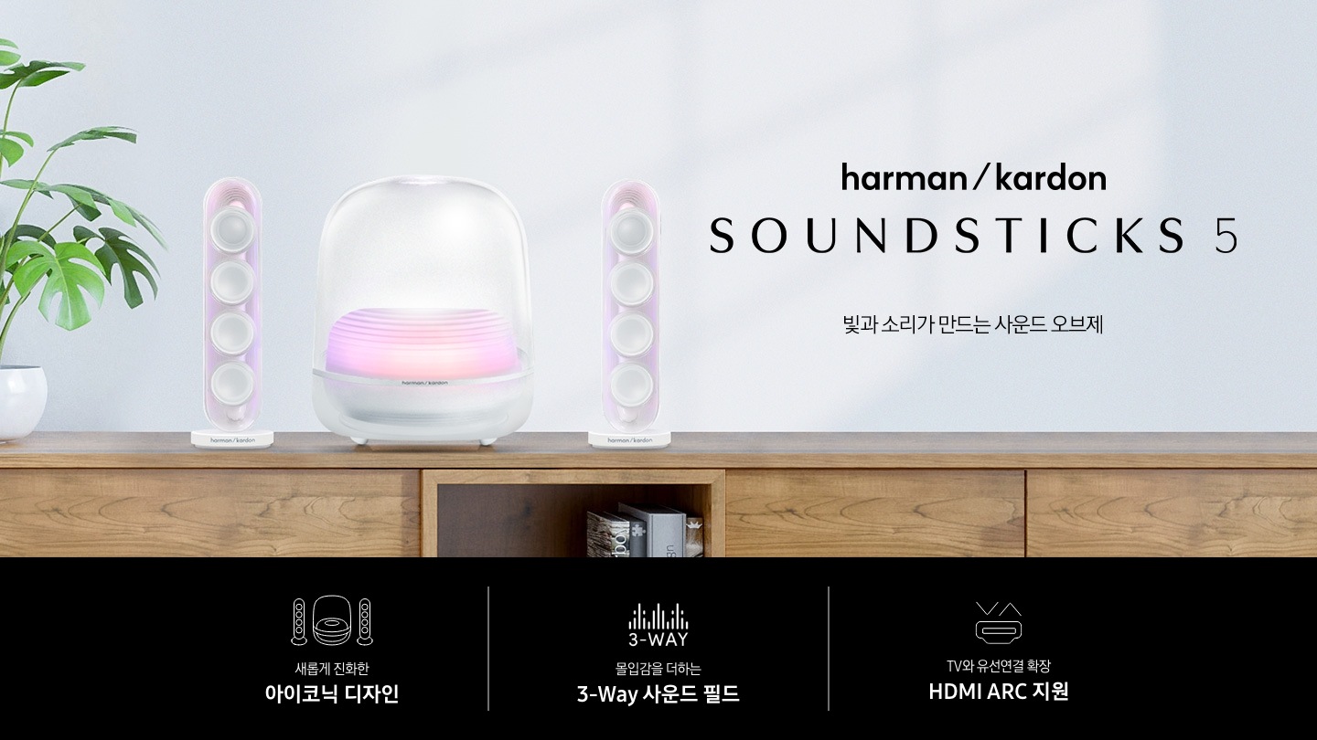 장식장 위에 흰색 스피커가 놓여 있습니다. 스피커 왼쪽에는 화분이 놓여 있으며, 오른쪽에는 하만카돈 로고와 스피커의 모델명 ‘SOUND STICKS 5’와 ‘빛과 소리가 만드는 사운드 오브제‘ 문구가 기재되어 있습니다. 이미지 하단에는 ‘새롭게 진화한 아이코닉 디자인‘, ‘몰입감을 더하는 3-Way 사운드 필드‘, ‘TV와 유선연결 확장 HDMI ARC 지원’ 문구와 아이콘이 있습니다.