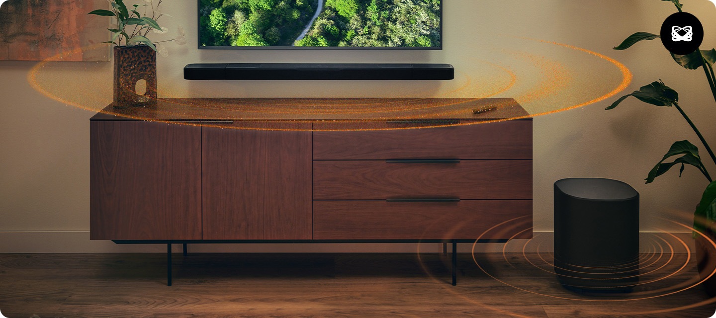 벽에 TV와 사운드바가 설치되어 있으며, 사운드바 아래에는 장식장이 놓여 있습니다. 장식장 오른쪽 옆에는 서브우퍼가 놓여 있습니다. 사운드바와 서브우퍼에서는 음향효과가 나오고 있습니다.