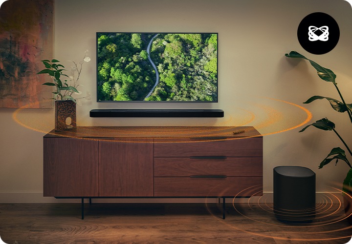 벽에 TV와 사운드바가 설치되어 있으며, 사운드바 아래에는 장식장이 놓여 있습니다. 장식장 오른쪽 옆에는 서브우퍼가 놓여 있습니다. 사운드바와 서브우퍼에서는 음향효과가 나오고 있습니다.