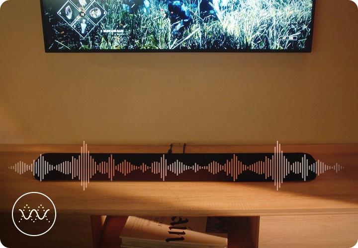 벽에는 TV가 설치되어 있으며, 그 아래에는 블랙 색상의 사운드바가 놓인 장식장이 있습니다. 사운드바 위로 음향효과가 나오고 있습니다.