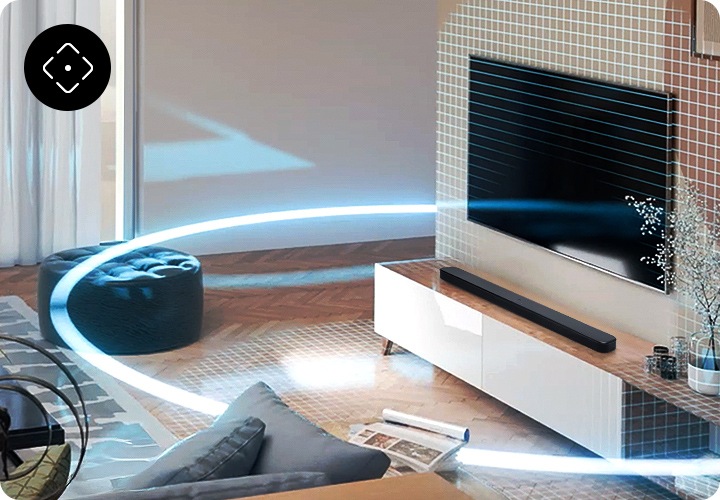 장식장 위에 블랙 색상의 사운드바가 놓여 있습니다. 장식장 앞에는 테이블과 소파가 놓여 있으며, 장식장 위로는 TV가 벽에 설치되어 있습니다. 사운드바에서 나온 소리가 거실을 감싸듯 음향효과가 표현되고 있습니다.