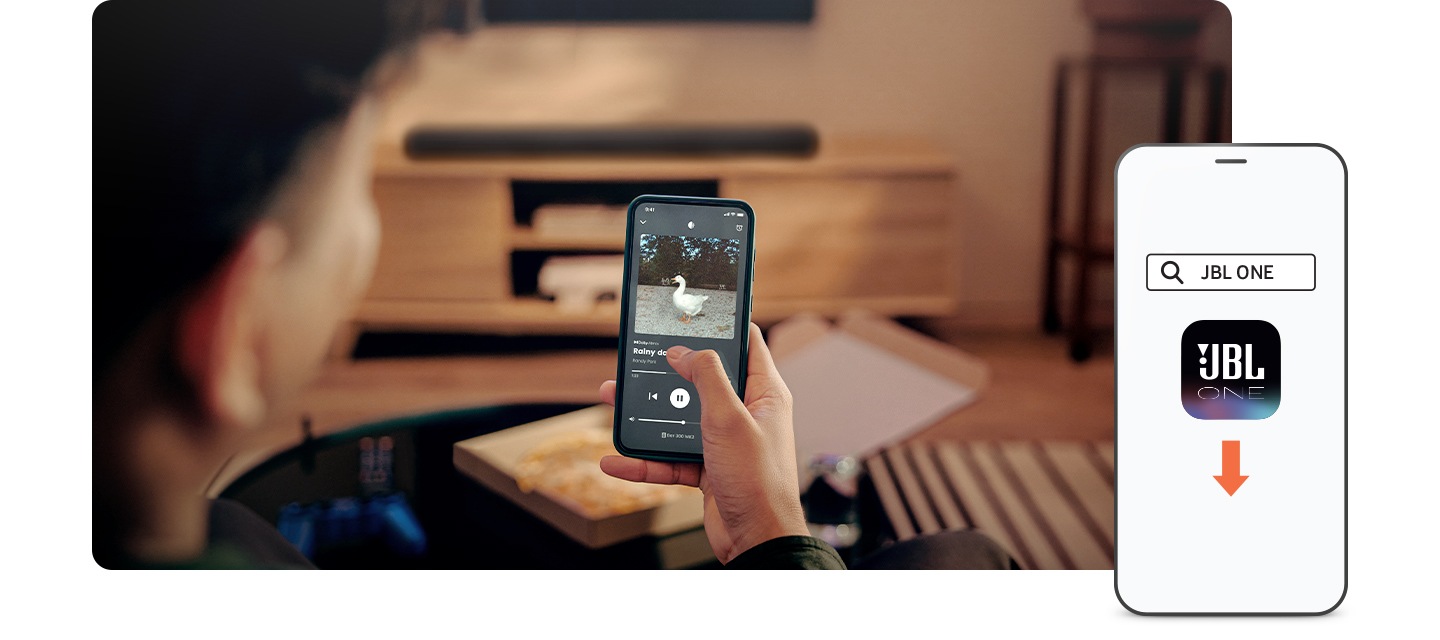 남성이 휴대폰으로 음악을 재생하고 있습니다. 남성 앞에는 블랙 색상의 사운드바가 놓여 있는 장식장이 보입니다. 이미지 오른쪽 하단에는 JBL One 앱 아이콘이 화면에 보이는 휴대폰이 놓여 있습니다.