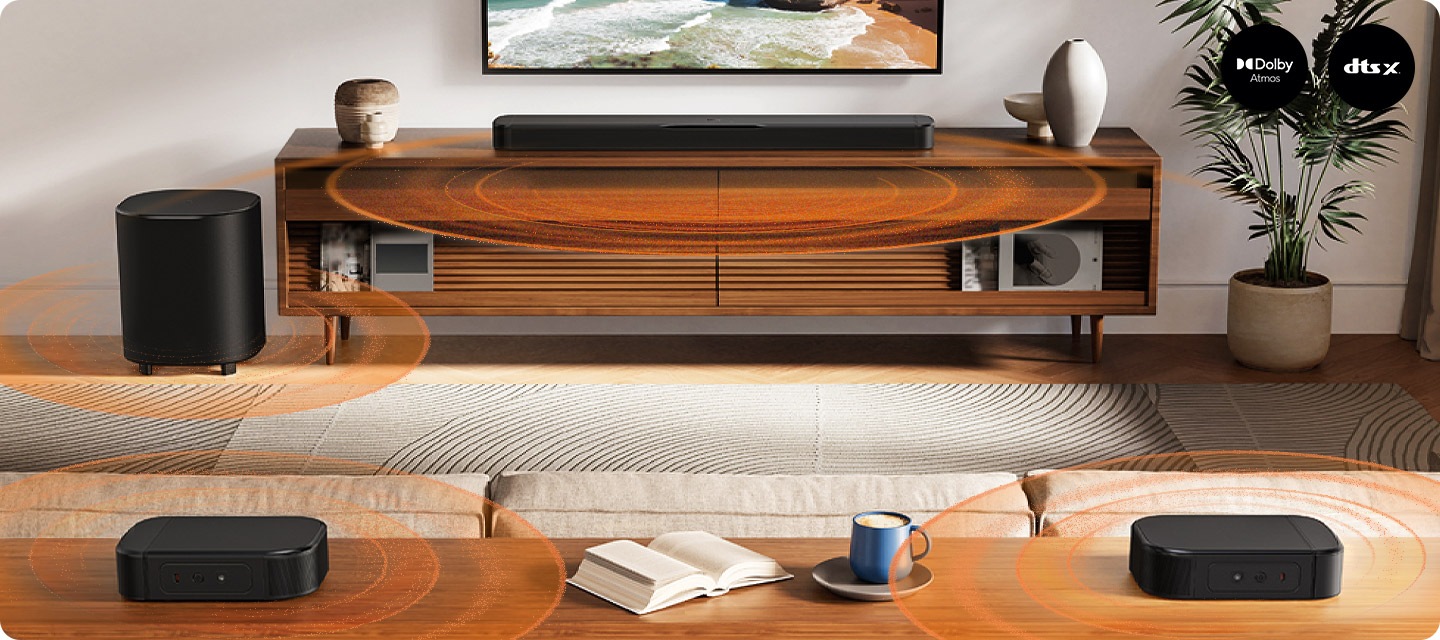 거실 벽에는 TV가 설치되어 있으며, 그 아래에는 스피커와 장식품이 놓인 장식장이 보입니다. 장식장 왼쪽에는 서브우퍼가 놓여 있으며, 오른쪽에는 화분이 놓여 잇습니다. 장식장 앞에는 소파가 놓여 있으며, 그 뒤에는 리어스피커가 놓인 장식장이 있습니다. 사운드바와 서브우퍼, 리어스피커에서는 음향효과가 나옵니다.