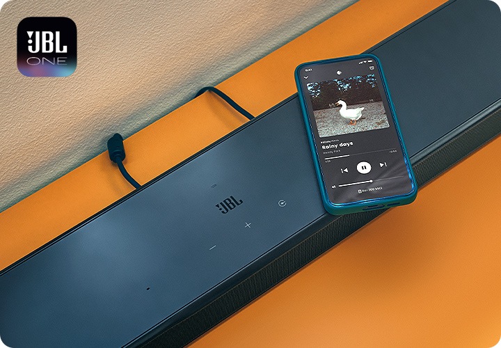 장식장 위에는 사운드바가 놓여 있습니다. 그 위에는 음악이 나오는 휴대폰이 놓여 있습니다.