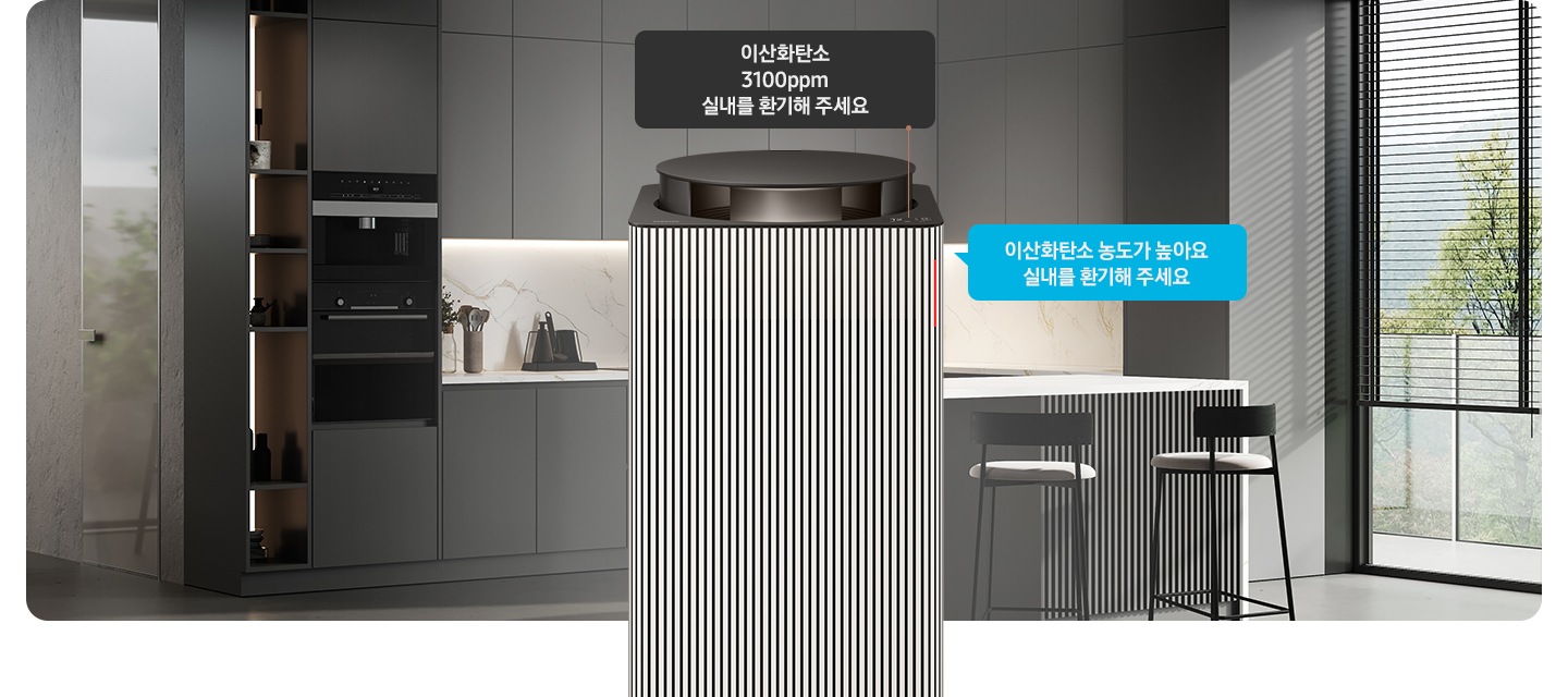 그레이 톤의 주방 전경을 배경으로 오른쪽에는 아일랜드 식탁 의자 2개와 블라인드가 내려진 커다란 창문이 놓여 있습니다. 이미지 가운데에 Infinite AI 공기청정기 상단부가 확대되어 보입니다. 공기청정기 상단에는 알림 창 부분이 이산화탄소 3100ppm 실내를 환기해 주세요. 가 확대되어 놓여 있고 공기청정기 오른쪽으로 음성 안내를 표시하는 파란색 말풍선 안에 이산화탄소 농도가 높아요 실내를 환기해 주세요.라는 문구가 적혀 있습니다.
