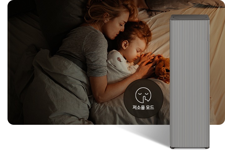 베이지 톤의 침구가 깔린 침대에 누워 회색 이불을 덮고 잠들어 있는 엄마와 아기의 옆모습이 있습니다. 오른쪽 하단에는 Infinite AI 공기청정기가 정면을 바라보고 서 있습니다. 공기청정기 왼쪽에는 검은색 원 안에 입을 가리는 모습을 한 사람 얼굴 아이콘이 있고 하단에는 저소음 모드라는 문구가 적혀 있습니다.