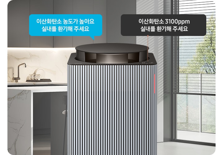 그레이 톤의 주방 전경을 배경으로 오른쪽에는 아일랜드 식탁 의자 2개와 블라인드가 내려진 커다란 창문이 놓여 있습니다. 이미지 가운데에 Infinite AI 공기청정기 상단부가 확대되어 보입니다. 공기청정기 상단에는 알림 창 부분이 이산화탄소 3100ppm 실내를 환기해 주세요. 가 확대되어 놓여 있고 공기청정기 오른쪽으로 음성 안내를 표시하는 파란색 말풍선 안에 이산화탄소 농도가 높아요 실내를 환기해 주세요.라는 문구가 적혀 있습니다.