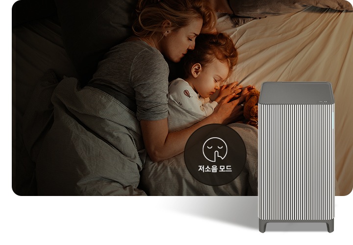 베이지 톤의 침구가 깔린 침대에 누워 회색 이불을 덮고 잠들어 있는 엄마와 아기의 옆모습이 있습니다. 오른쪽 하단에는 Infinite AI 공기청정기가 정면을 바라보고 서 있습니다. 공기청정기 왼쪽에는 검은색 원 안에 입을 가리는 모습을 한 사람 얼굴 아이콘이 있고 하단에는 저소음 모드라는 문구가 적혀 있습니다.