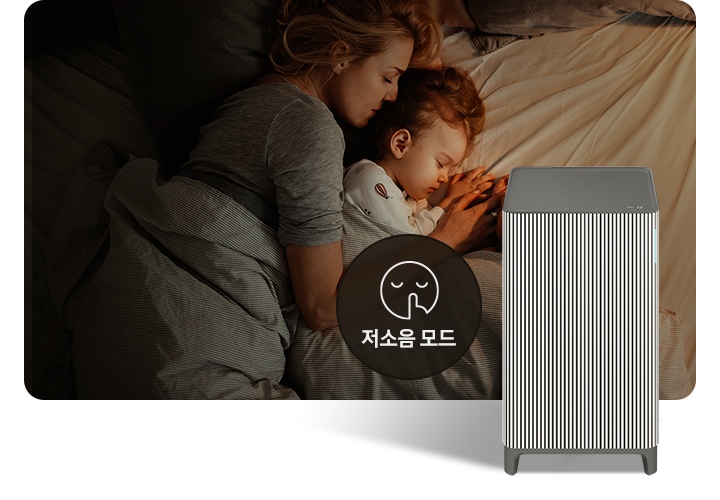 베이지 톤의 침구가 깔린 침대에 누워 회색 이불을 덮고 잠들어 있는 엄마와 아기의 옆모습이 있습니다. 오른쪽 하단에는 Infinite AI 공기청정기가 정면을 바라보고 서 있습니다. 공기청정기 왼쪽에는 검은색 원 안에 입을 가리는 모습을 한 사람 얼굴 아이콘이 있고 하단에는 저소음 모드라는 문구가 적혀 있습니다.