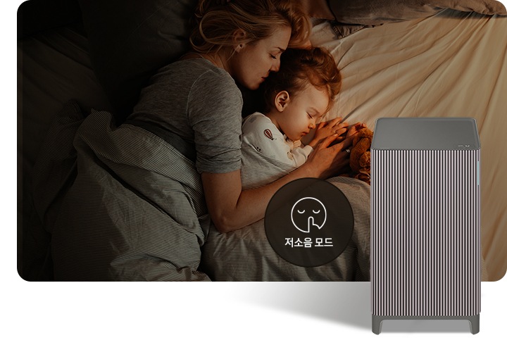 베이지 톤의 침구가 깔린 침대에 누워 회색 이불을 덮고 잠들어 있는 엄마와 아기의 옆모습이 있습니다. 오른쪽 하단에는 Infinite AI 공기청정기가 정면을 바라보고 서 있습니다. 공기청정기 왼쪽에는 검은색 원 안에 입을 가리는 모습을 한 사람 얼굴 아이콘이 있고 하단에는 저소음 모드라는 문구가 적혀 있습니다.