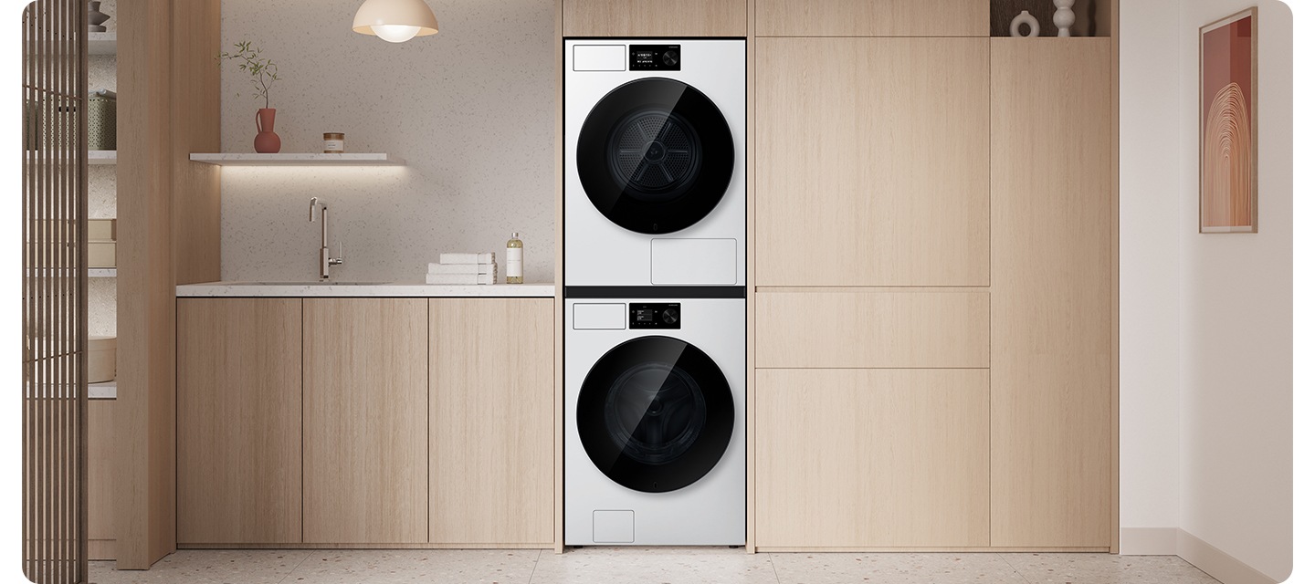 밝은 우드톤 붙박이장에 건조기&세탁기 패키지가 직렬로 설치되어 있습니다. 좌측 하부장 위에는 수건 등의 오브제가 놓여있는 연출된 이미지입니다.