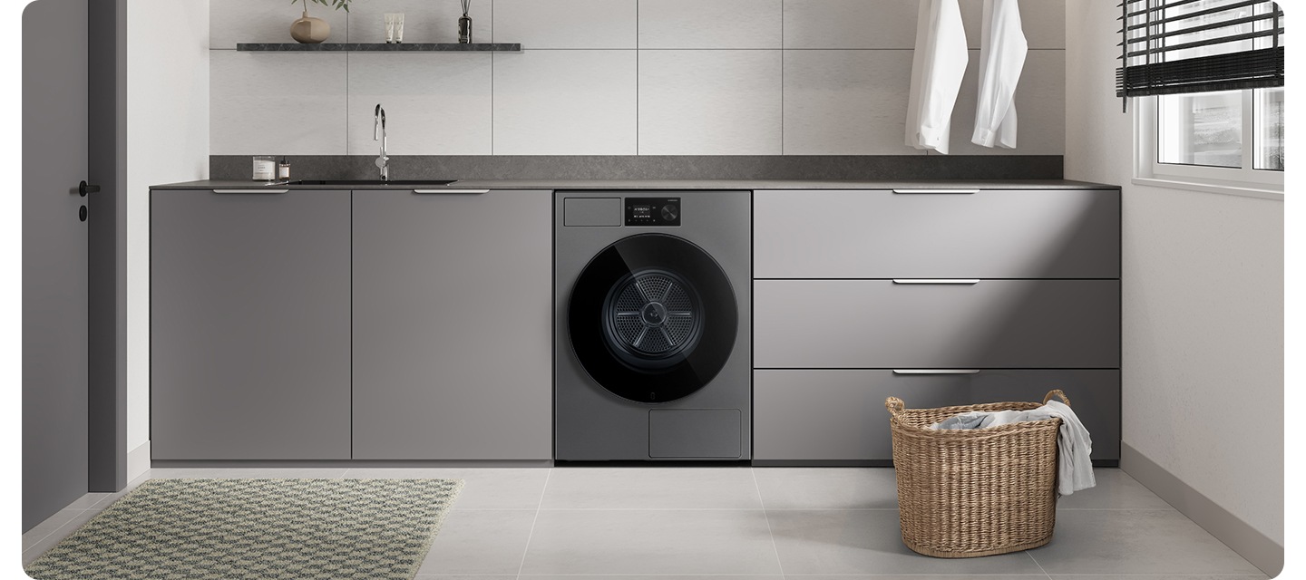 화이트&그레이톤 인테리어컷으로 그레이톤 하부장 중앙에 Bespoke AI 건조기가 설치되어 있습니다. 상부장 부분에는 싱크대와 수전이 있고 앞쪽에는 라탄 바구니에 옷감이 들어있는 연출된 이미지입니다.