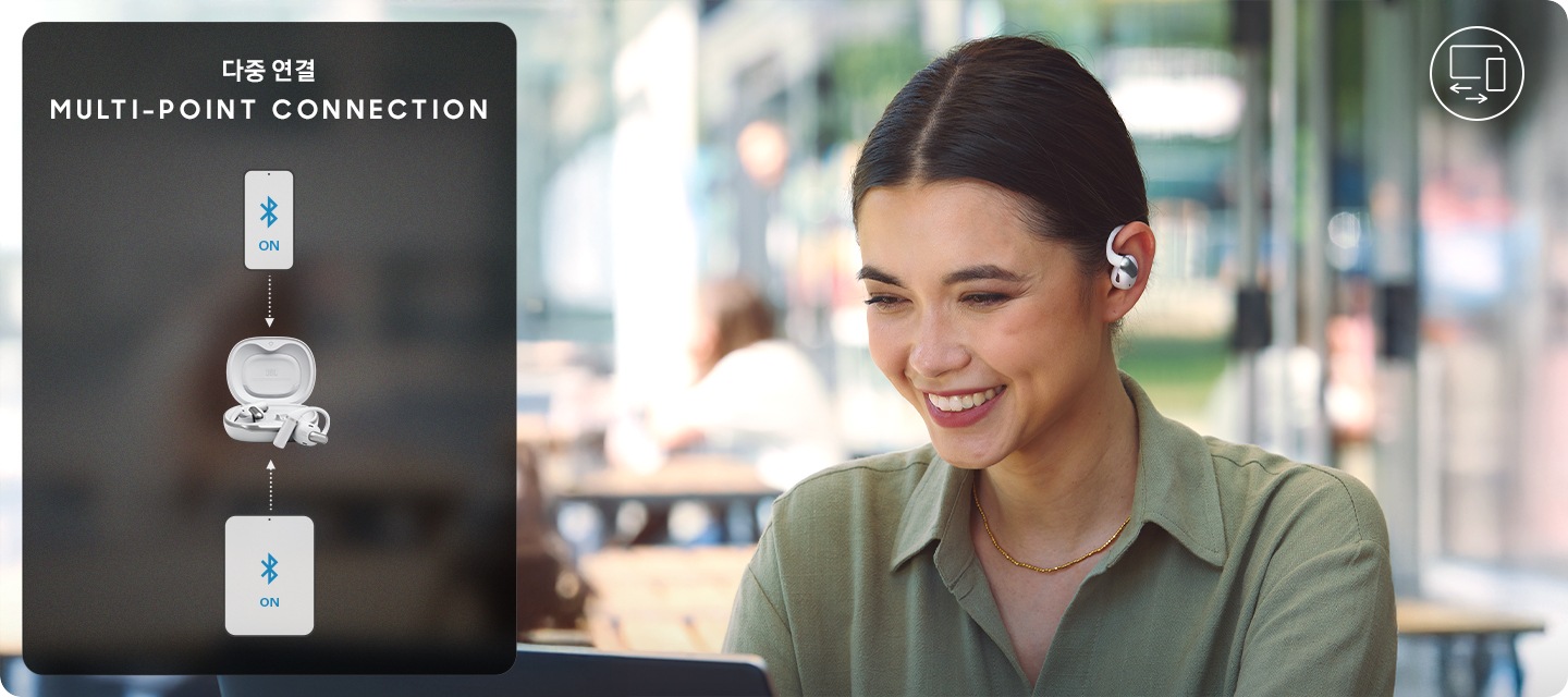 화이트 색상의 이어폰을 착용한 여성이 카페 테라스 앉아서 노트북을 바라 보고 있습니다. 여성 왼쪽에는 이어폰이 휴대폰과 태블릿에 연결되어 있습니다.