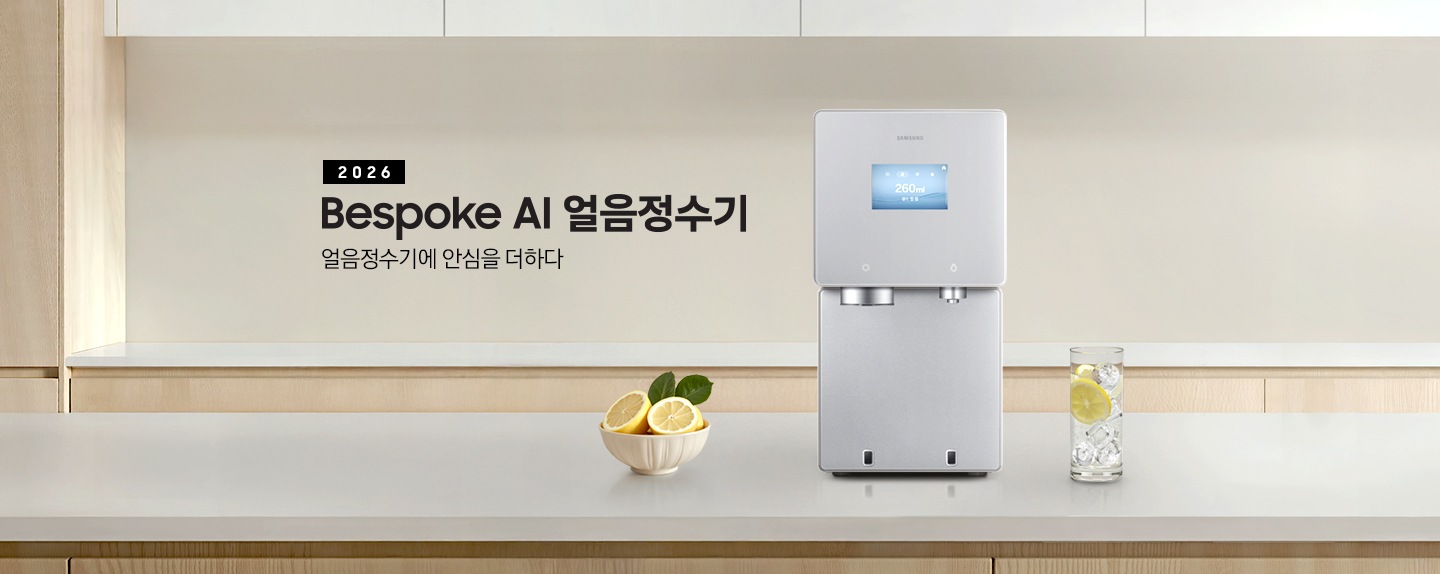 2026 Bespoke AI 얼음정수기. 얼음정수기에 안심을 더하다. 하얀색 대리석 테이블 위에 얼음정수기 사틴 베이지 컬러가 정면을 보고 설치되어 있습니다. 좌측에는 레몬이 가득 담긴 그릇이 있고 우측에는 얼음이 가득 담긴 물컵에 레몬슬라이스가 들어있습니다.