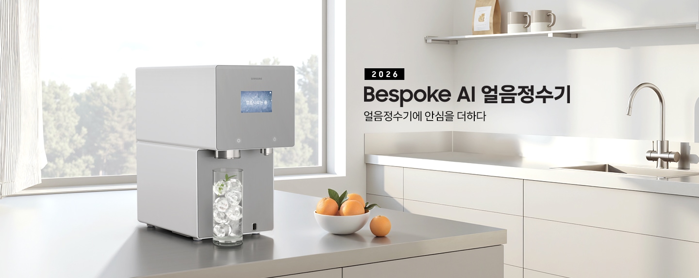 2026 Bespoke AI 얼음정수기. 얼음정수기에 안심을 더하다.  회색 테이블 위에 얼음정수기 사틴 그레이지 컬러가 설치되어 있는 측면 이미지 입니다. 정수기 얼음 토출구 아래에는 얼음이 가득 든 물컵이 놓여있습니다. 정수기 우측에는 오렌지가 가득 담긴 그릇이 놓여있습니다.