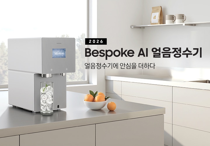 2026 Bespoke AI 얼음정수기. 얼음정수기에 안심을 더하다.  회색 테이블 위에 얼음정수기 사틴 그레이지 컬러가 설치되어 있는 측면 이미지 입니다. 정수기 얼음 토출구 아래에는 얼음이 가득 든 물컵이 놓여있습니다. 정수기 우측에는 오렌지가 가득 담긴 그릇이 놓여있습니다.